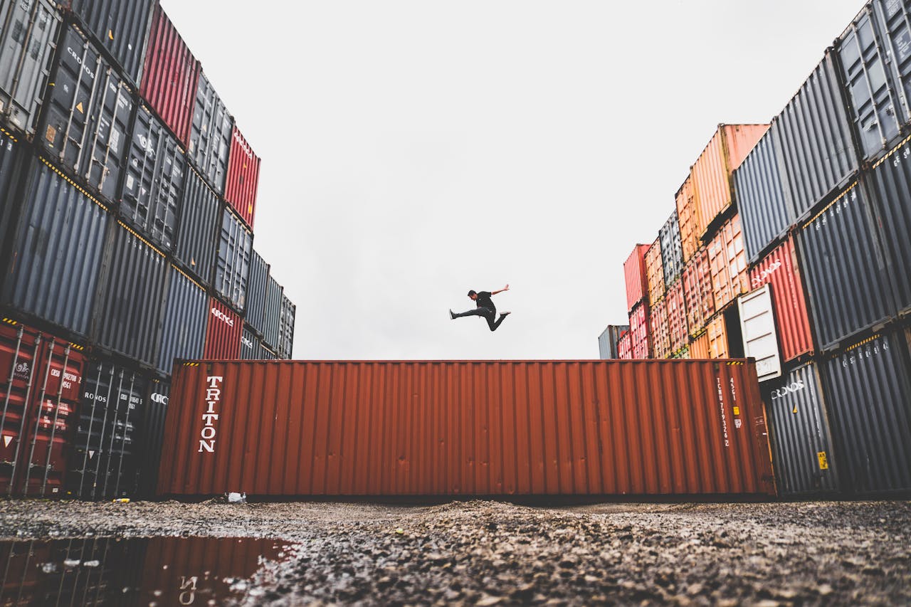 about-me-img A person leaps dramatically above stacked shipping containers, showcasing freedom and industrial energy.